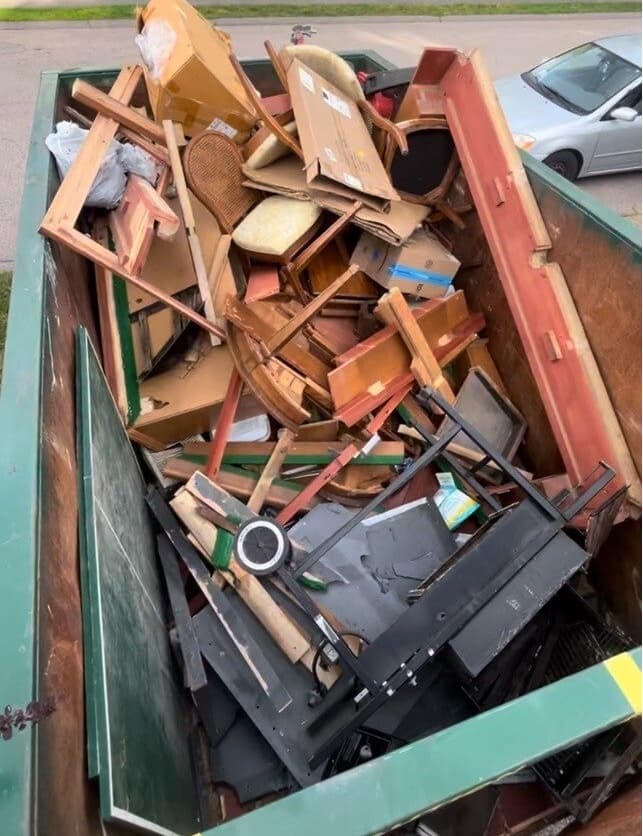 A dumpster filled with broken furniture and debris